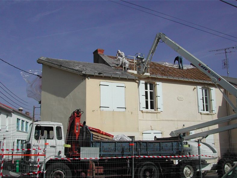 Camion-grue et nacelle devant une maison pendant le retrait de sa toiture