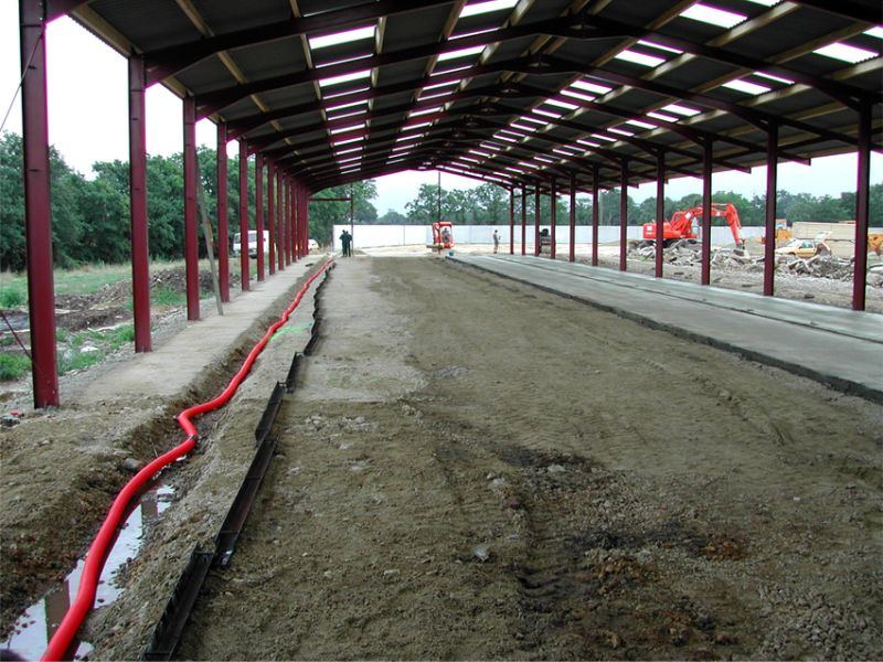 Intérieur d'une stabulation en construction, tranchée de réseau sous la charpente