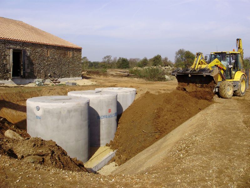 Cuves en béton posées près d'une maison, pelle jaune en fouille
